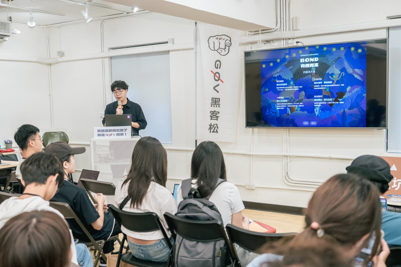 g0v 黑客松的參與者在座位上觀看 Bond 團隊公開發表，前方投影可見 BOND 標誌。