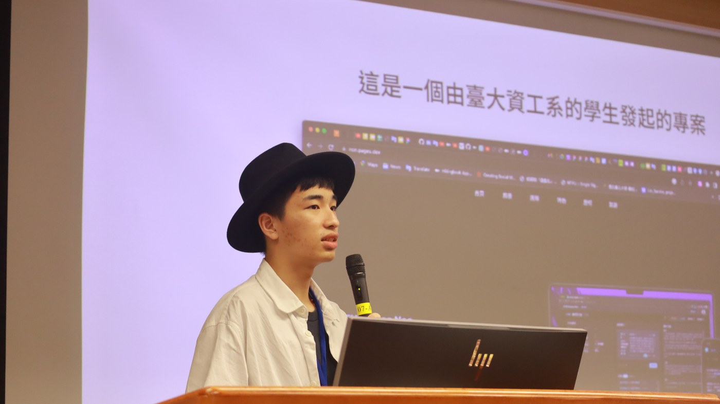 王豆腐戴黑帽、穿白襯衫，站在講台後持麥克風分享，身後投影介紹由臺大資工學生發起的專案。